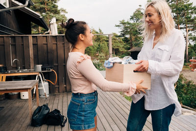 Smiling young woman giving wooden container to friend