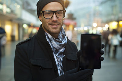 Portrait of young man showing digital tablet standing outdoors