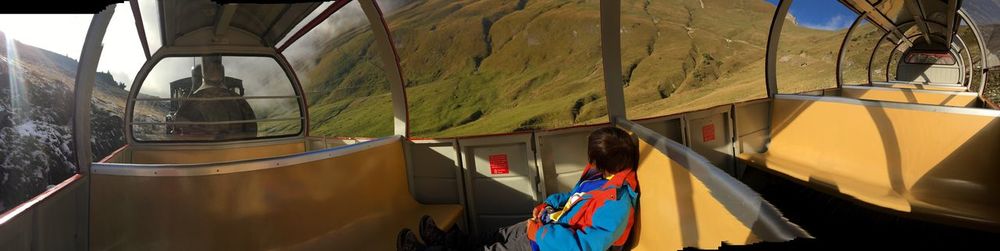 Panoramic view of boy sitting in train by mountain