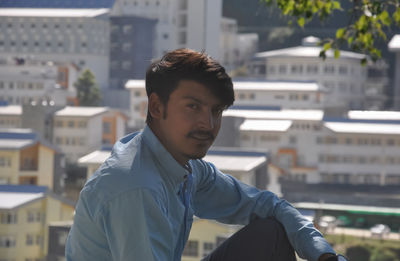 Closeup of a young guy looking at camera sitting outside with buildings in background