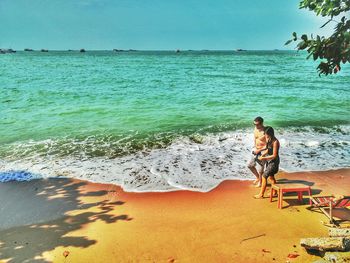 Shirtless man with woman walking at beach on sunny day