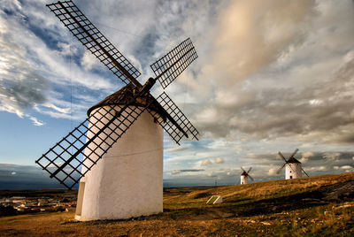 Windmills on field against cloudy sky