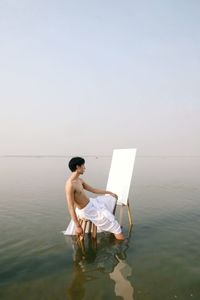 Rear view of woman sitting on rock by sea