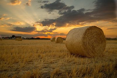 Hay bales on field against sky during sunset