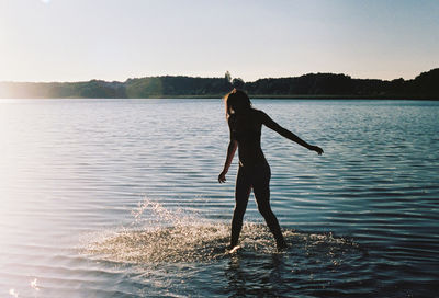 Rear view of woman standing in lake against sky