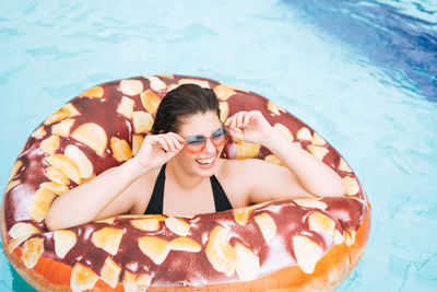 Happy young woman plus size body positive in inflatable doughnut circle swimming in pool