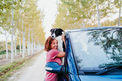 Side view of woman embracing dog through car window
