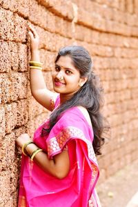 Side view portrait of smiling young woman wearing pink sari by wall