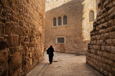 Rear view of man walking on footpath against building