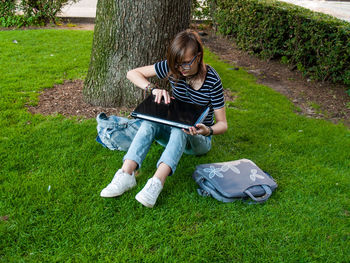 Teenage girl using laptop while sitting on grassy field