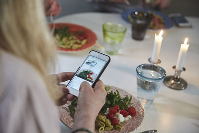 Cropped image of woman photographing food through smart phone at dining table