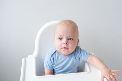 Portrait of cute baby boy sitting against white wall