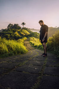 Young man standing on road by trees against sky