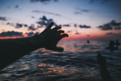 Human hand against sky during sunset