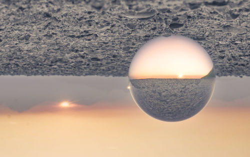 Close-up of crystal ball on beach against sky during sunset