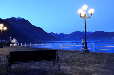 Illuminated street light by sea against clear sky at night