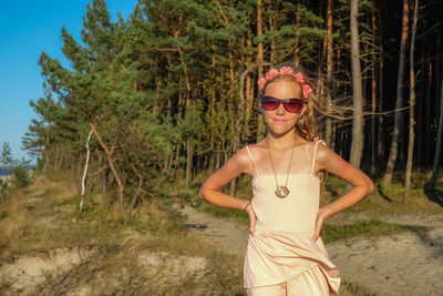 Portrait of young woman wearing sunglasses standing by tree