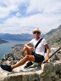 Portrait of mature man sitting on mountain against sky