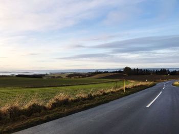 Empty road amidst field against sky