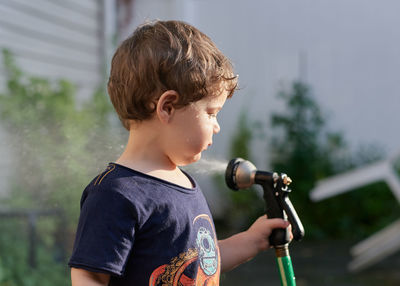 Little boy playing with a watering hose in the backyard