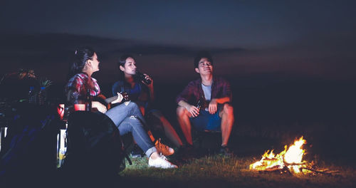 People sitting on bonfire against sky at night