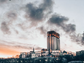 Factory by building against sky during sunset