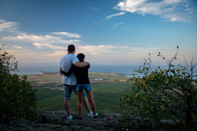 Rear view of couple standing with arms around against landscape