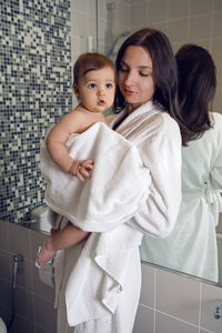Mother in a bathrobe and with a child standing in the bathroom