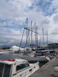 Boats in harbor against cloudy sky