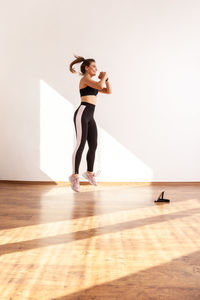 Full length of woman sitting on hardwood floor against wall