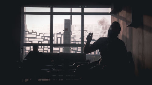 Rear view of silhouette man sitting on window