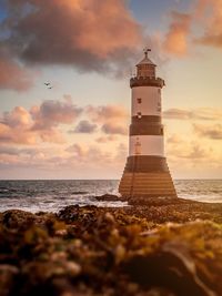 Lighthouse on beach against sky during sunset