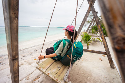 Rear view of man sitting on rope at beach against sky