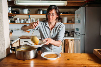 Housewife pouring delicious aromatic pumpkin cream soup into plate while serving dinner in home kitchen