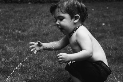 Side view of boy playing with sprinkler on grassy field