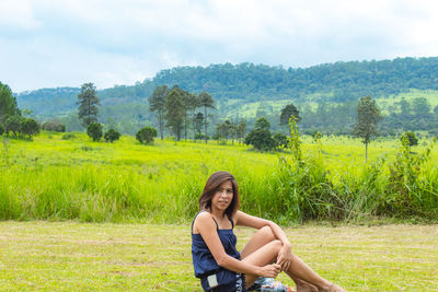 Full length portrait of woman sitting on grassy landscape