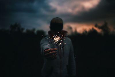 Close-up of silhouette hand holding sparkler against sky