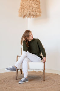 Young woman sitting on chair against wall