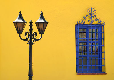 Vintage style gorgeous street lamp against yellow rough wall with a vibrant blue artistic window