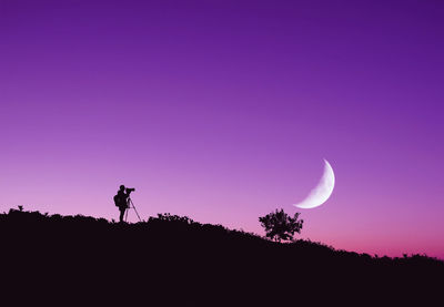 Low angle view of photographer standing on hill against purple sky