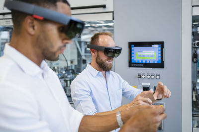 Two technicians wearing augmented reality glasses in a factory and gesturing