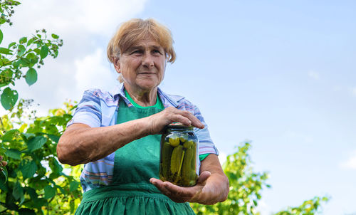 Portrait of smiling young woman holding plant against sky