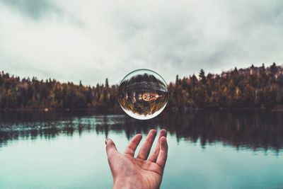 Close-up of hand holding crystal ball against calm lake