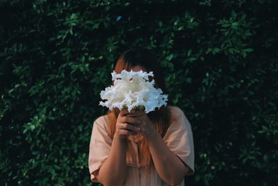 Midsection of person holding umbrella standing by flowering plants