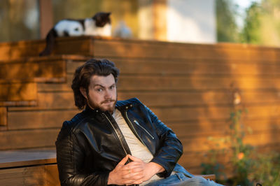  young bearded man in a  leather jacket sitting on the terrace  and looking thoughtfully at camera