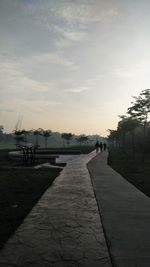 Empty footpath amidst trees against sky during sunset