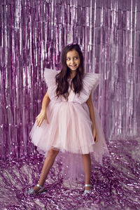 Beautiful girl with big eyes in a pink dress stands against the background of new year's tinsel