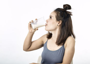Portrait of young woman drinking glass against white background