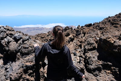 Rear view of woman standing on rock against sky