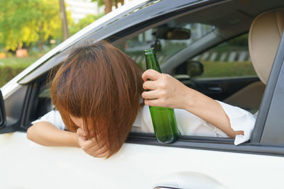 Woman holding green bottle while vomiting through car window